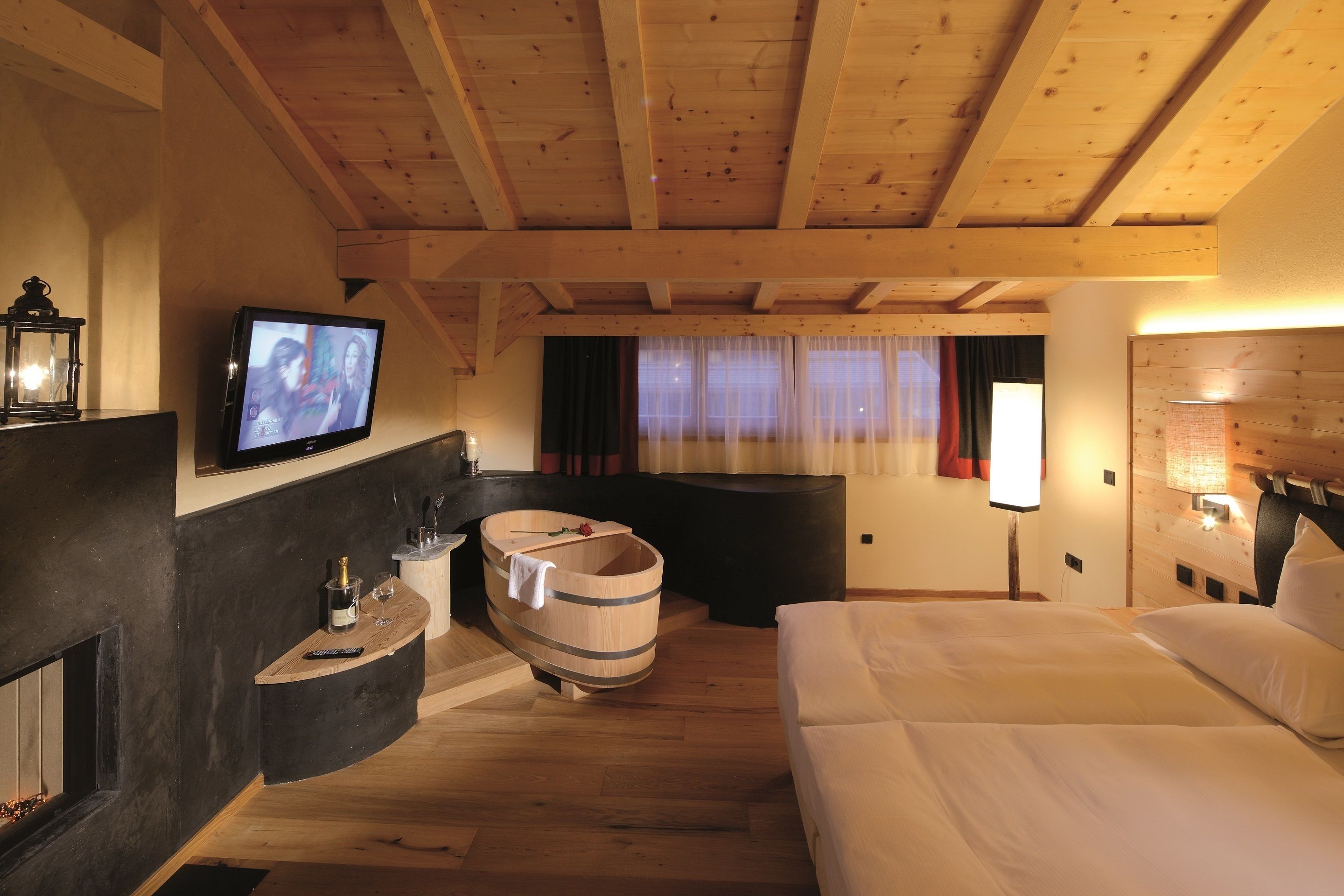 Ein gemütliches Zimmer mit Holzboden, Fernseher, Holzwanne, Sofa und Nachttisch mit Flasche und Gläsern.
