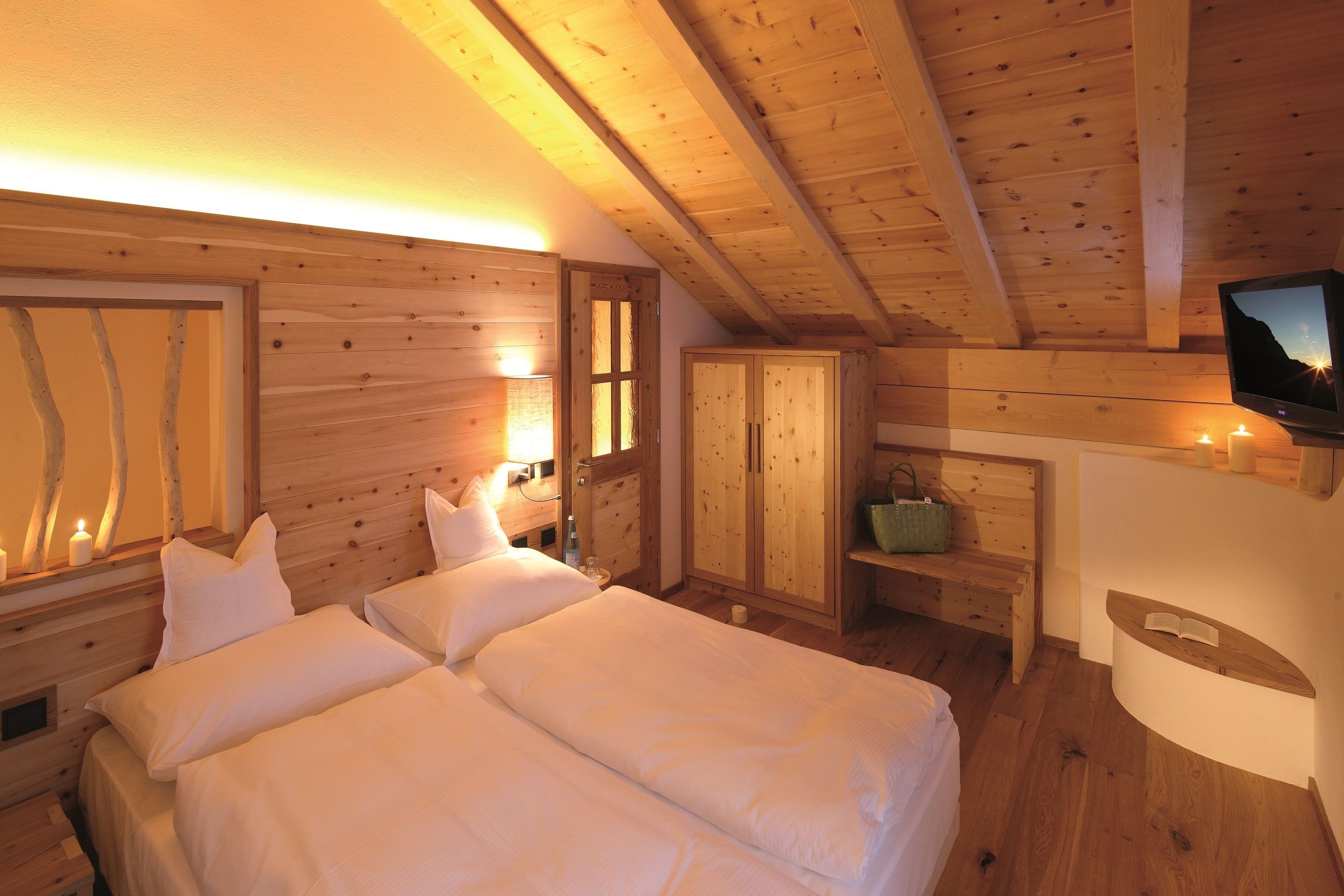 A wooden cabin bedroom with two beds, a television, and a small table with a candle.