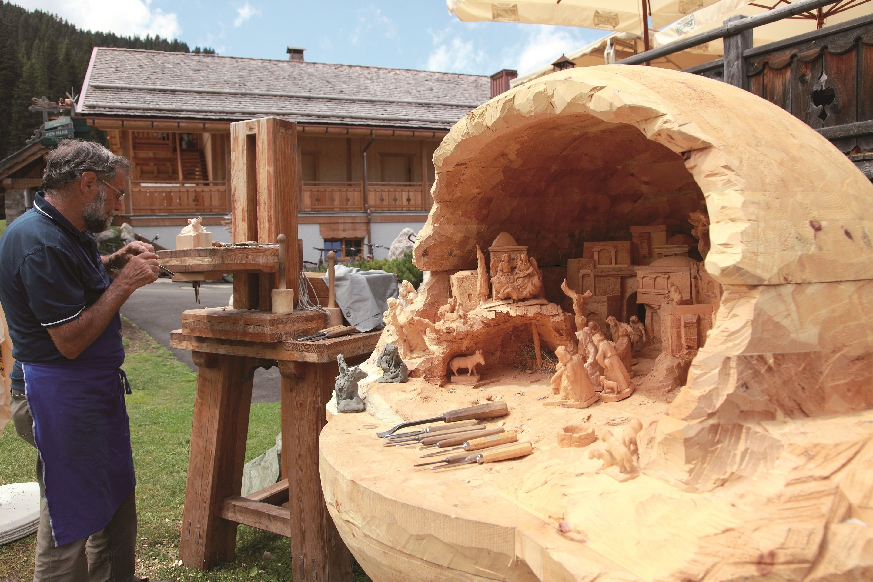 A woodworking workshop with a large wooden sculpture in progress, tools on the table, and a building in the background.