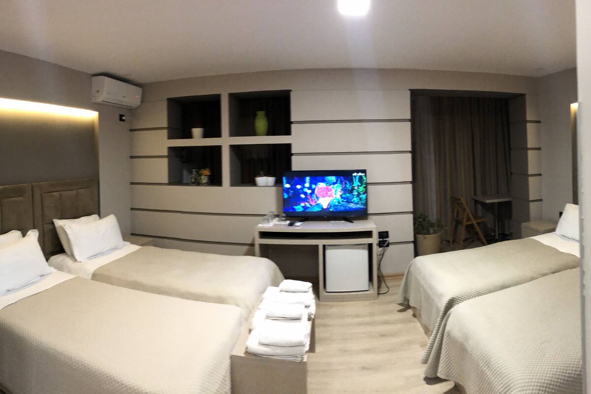 A hotel room with two beds, a TV, a small table, and a wall-mounted shelf.