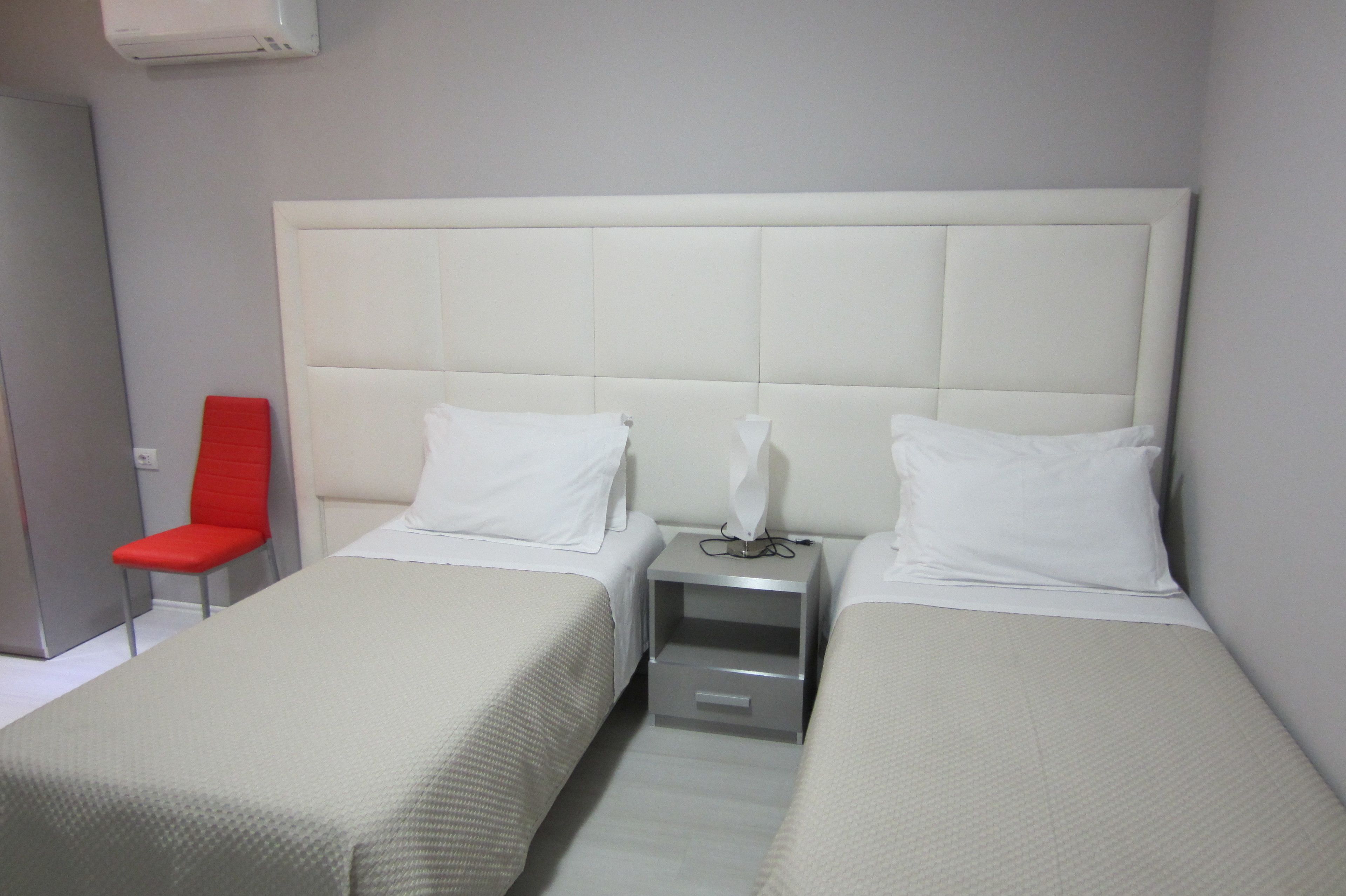 Una habitación de hotel con dos camas, una silla roja y una mesita de noche con lámpara.
