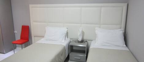 Una habitación de hotel con dos camas, una silla roja y una mesita de noche con lámpara.