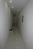 Un pasillo estrecho y bien iluminado con paredes blancas y piso brillante, que conduce a una puerta al final.