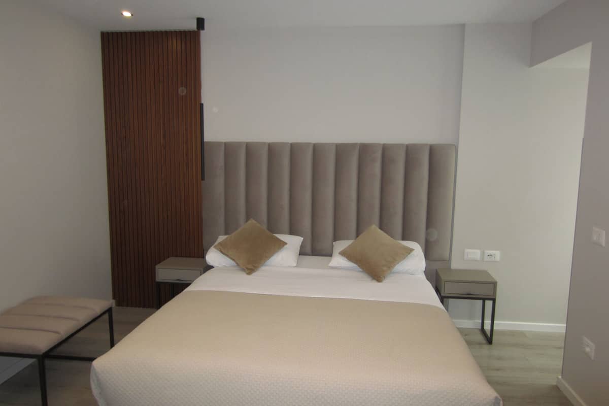 A modern hotel room with a large bed, two bedside tables, a wooden panel wall, and a neutral color scheme.