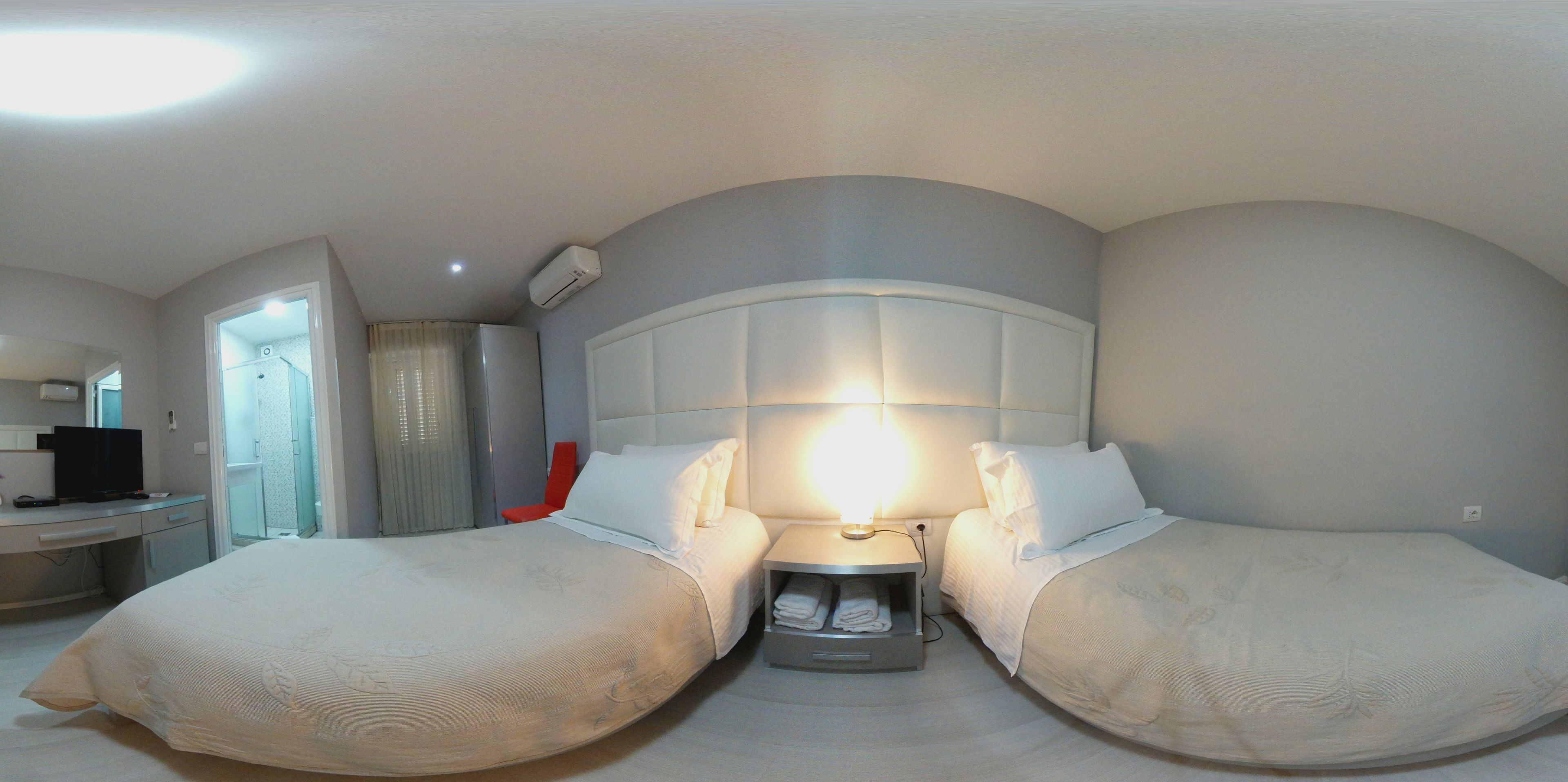 Une chambre d’hôtel avec deux lits, une table de chevet avec une lampe, une télévision et une salle de bain avec douche et toilettes.