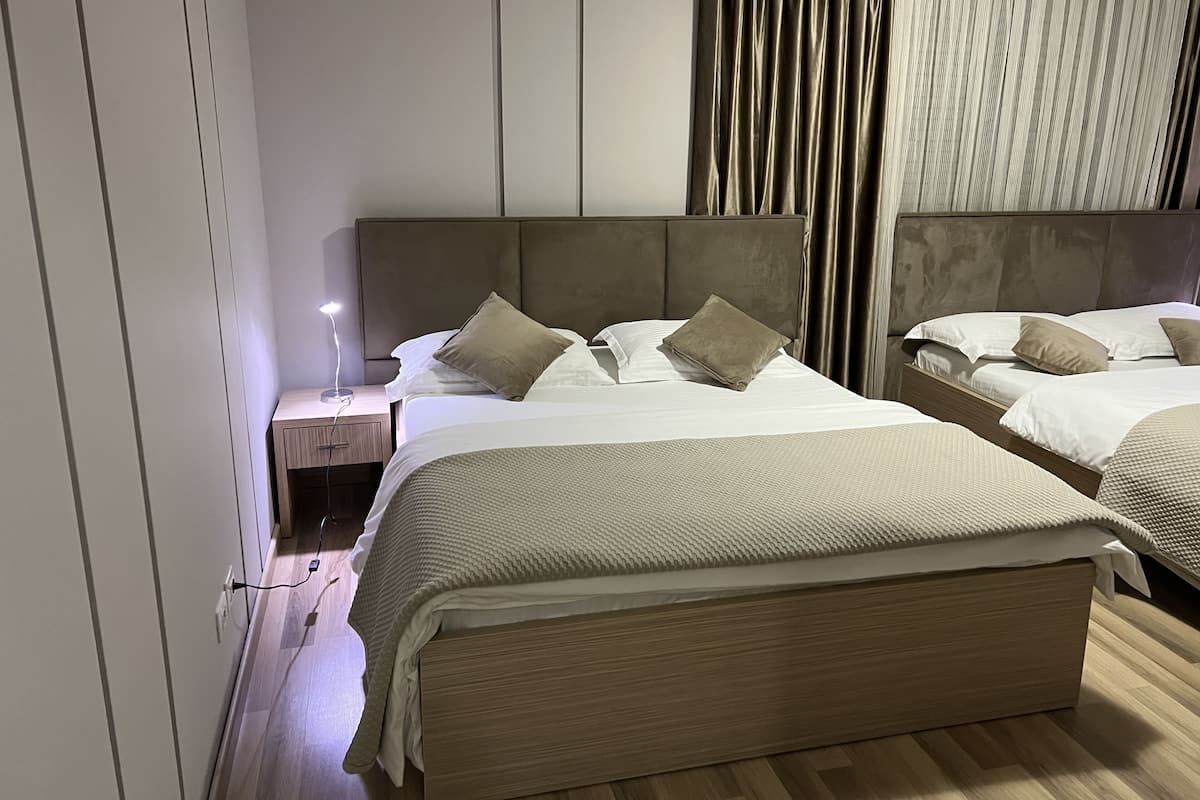 A hotel room with two beds, a nightstand with a lamp, and a window with curtains.