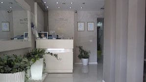 Un área de recepción con un mostrador blanco, plantas en macetas, certificados enmarcados en la pared y un diseño moderno y limpio.