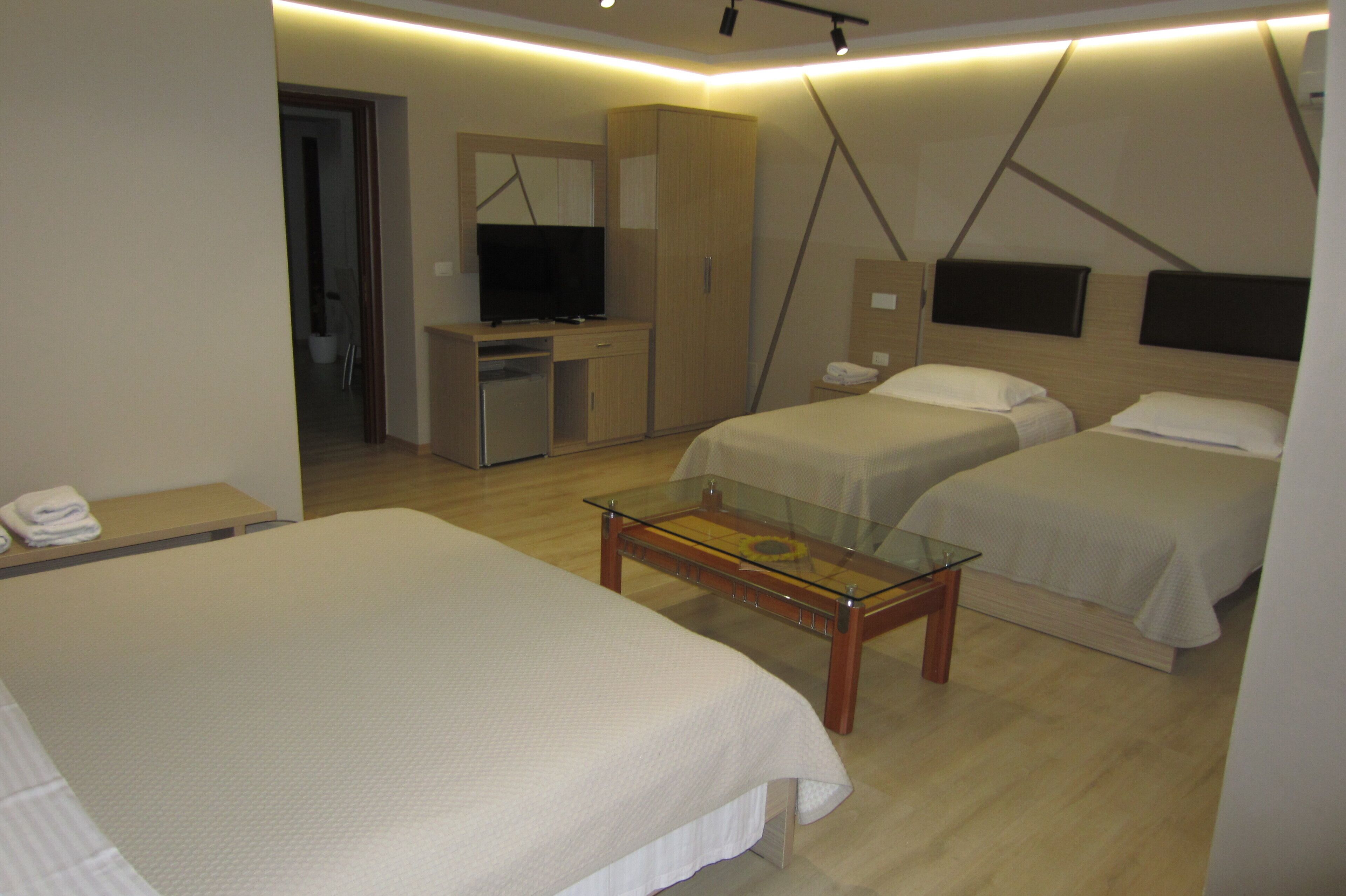 A hotel room with two beds, a desk with a television, and a glass coffee table.