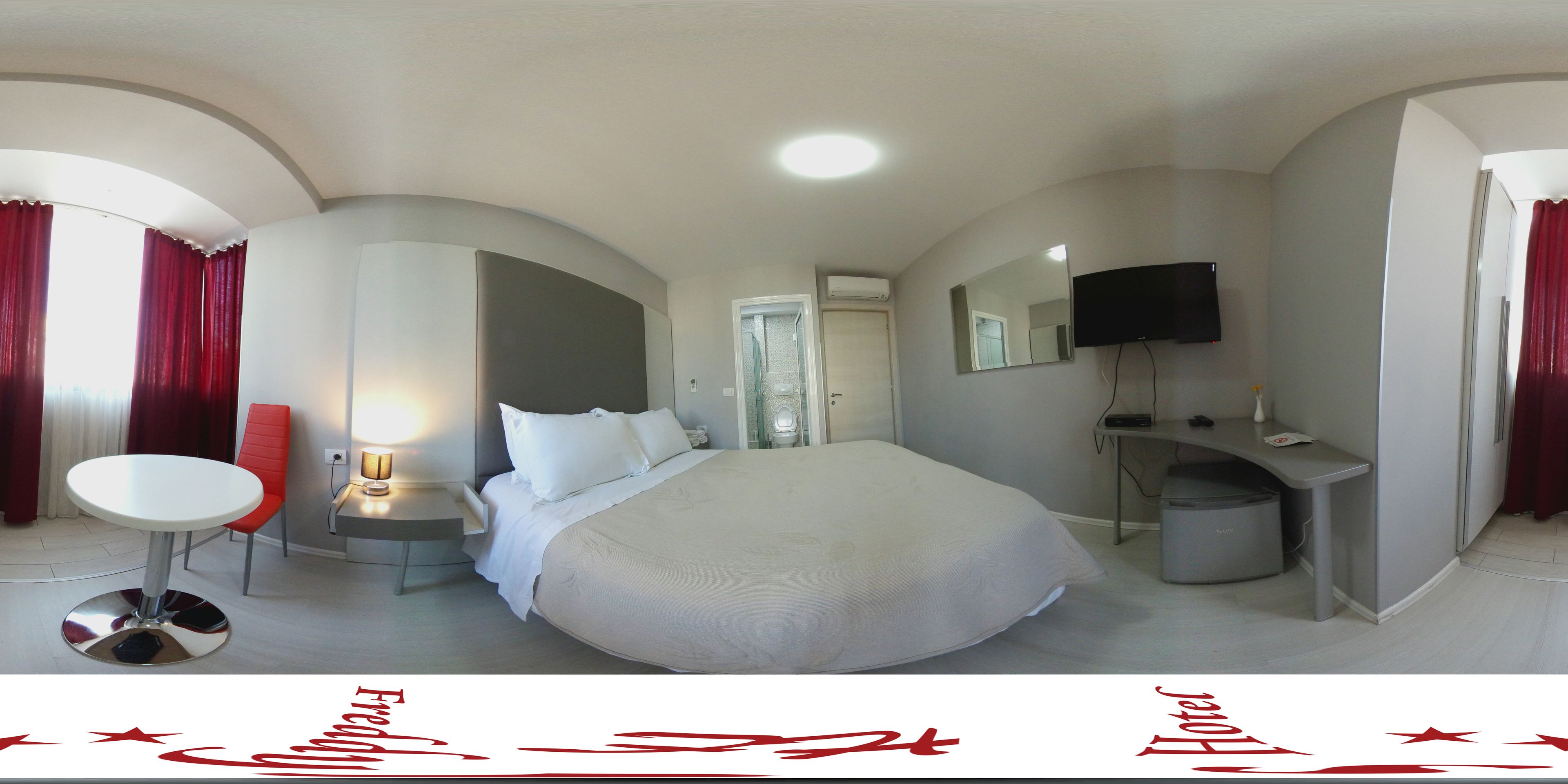Ein Hotelzimmer mit einem großen Bett, einem Schreibtisch, einem Sessel, einem Fernseher und einem Fenster mit Vorhängen.