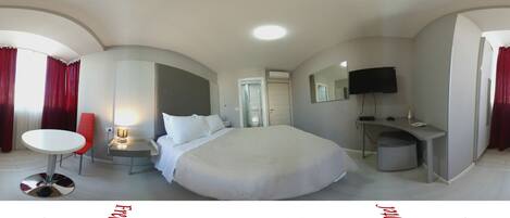 Ein Hotelzimmer mit einem großen Bett, einem Schreibtisch, einem Sessel, einem Fernseher und einem Fenster mit Vorhängen.