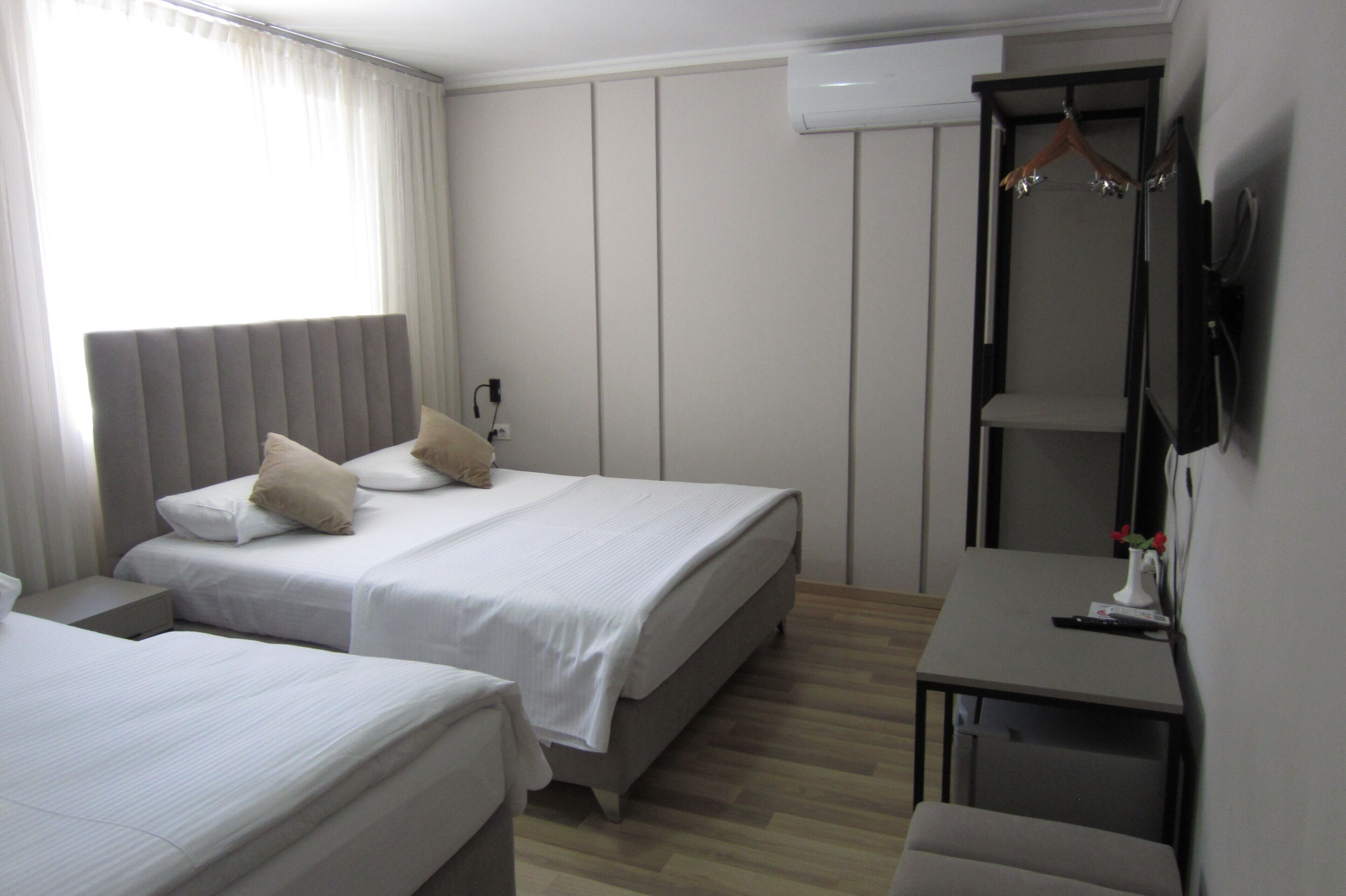 A hotel room with two beds, a desk, a wardrobe, and a TV.