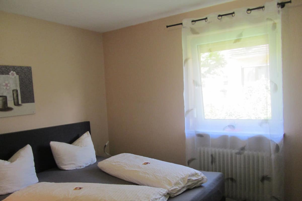 A bedroom with two beds, white bedding, a headboard, a window with sheer curtains, and a wall-mounted picture.