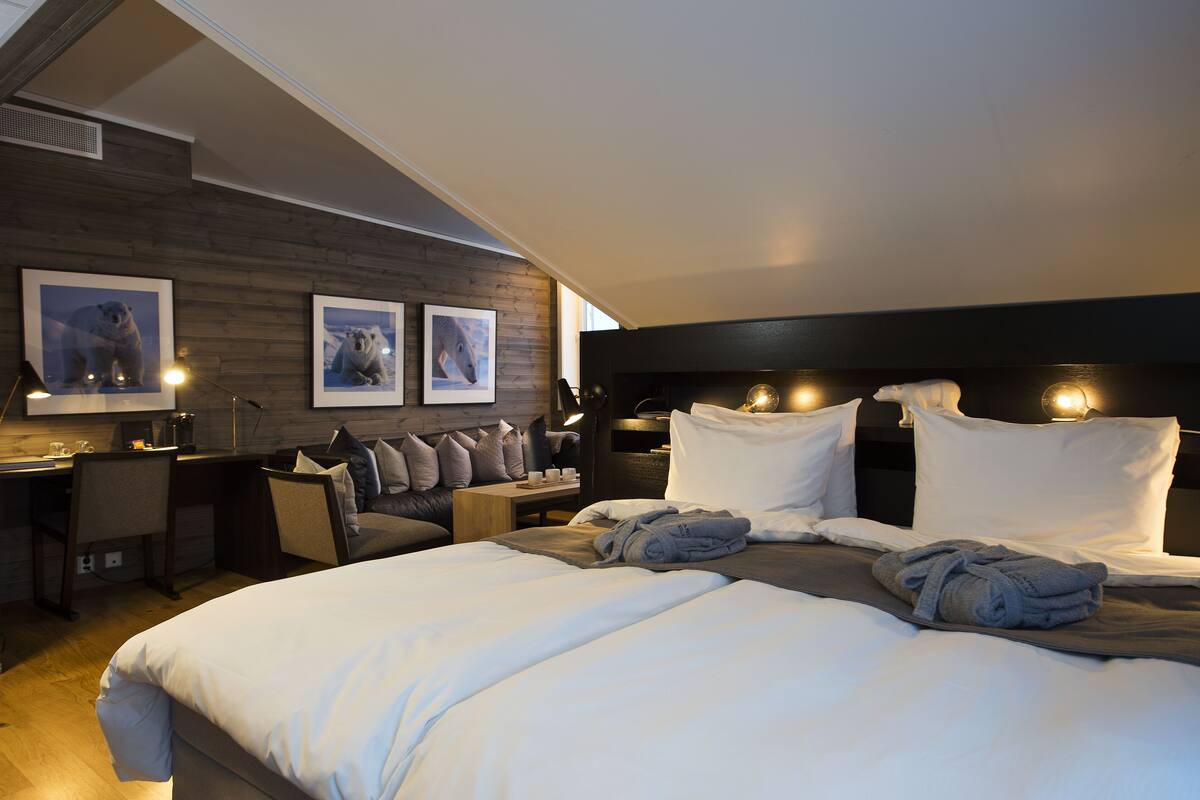 A modern hotel room with a large bed, a desk, and two framed pictures on the wall.