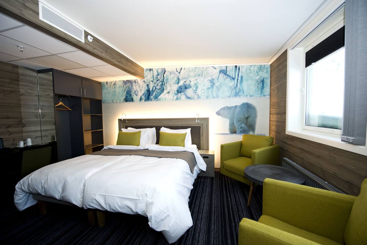 A hotel room with a bed, a seating area with chairs, a small table, a coat rack, and a large window.