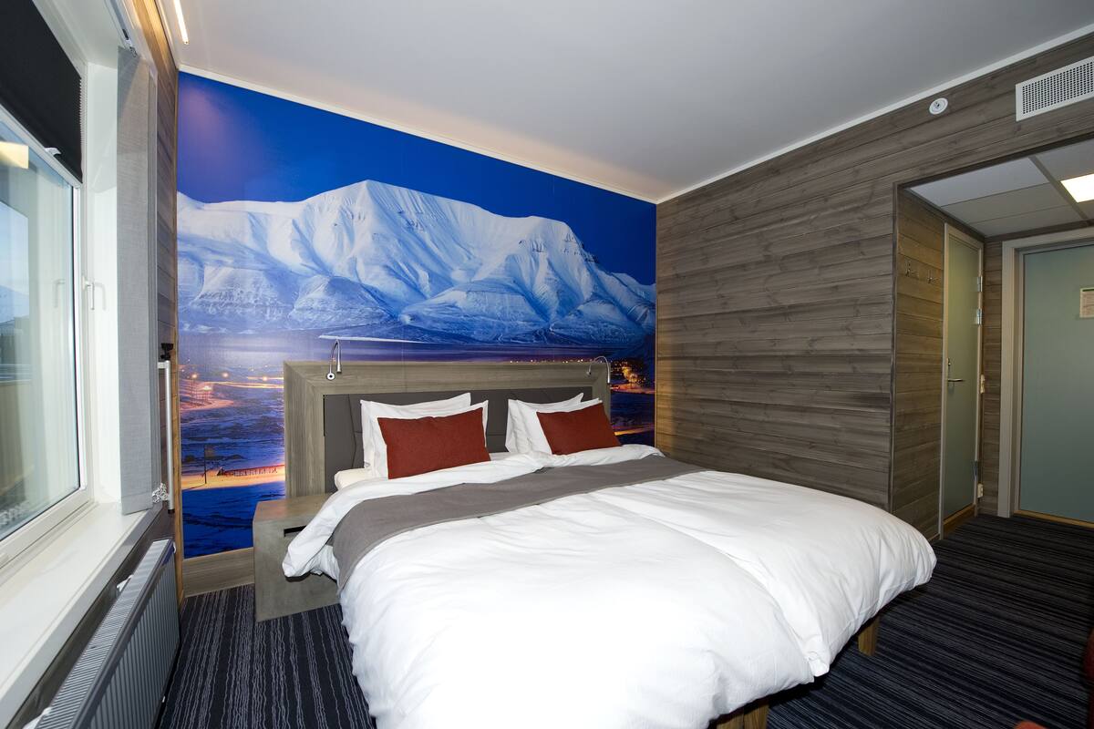 A hotel room with a large bed, a view of a snowy mountain through a window, and a wooden wall.