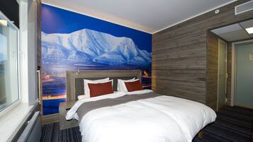 A hotel room with a large bed, a view of a snowy mountain through a window, and a wooden wall.