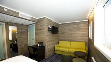 Una habitación de hotel con una cama, un sofá amarillo, una mesita y un televisor montado en la pared.