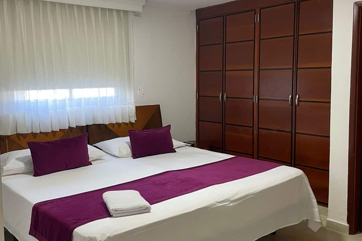 Quarto de hotel com cama grande, guarda-roupa e janela com cortinas.