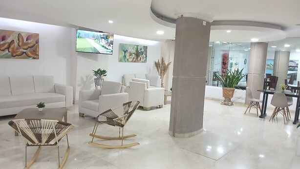 A modern lobby with white sofas, a dining area, and a TV screen. - Hotel Charthon (Barranquilla)