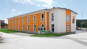 Hotel entrance with a flat roof and symmetrical windows, set amidst a well-manicured lawn and parking area.
