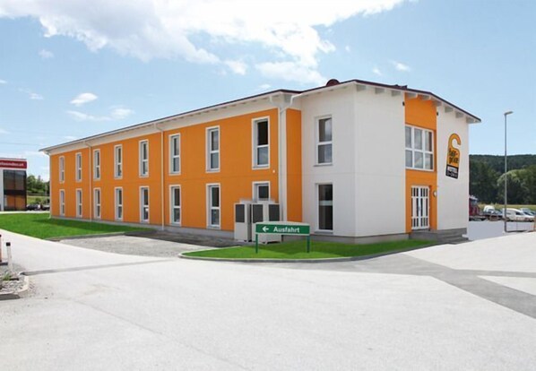 A two-story building with orange and white exterior walls, a sign indicating an exit, and a parking lot in the foreground. - Fair-Price-Hotel (Bad Waltersdorf)