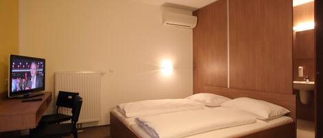 Habitación de hotel con cama, escritorio con televisor, silla y aire acondicionado instalado en la pared.