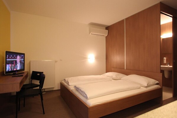 A hotel room with a bed, a desk with a TV, a chair, and a wall-mounted air conditioner. - Fair-Price-Hotel (Bad Waltersdorf)