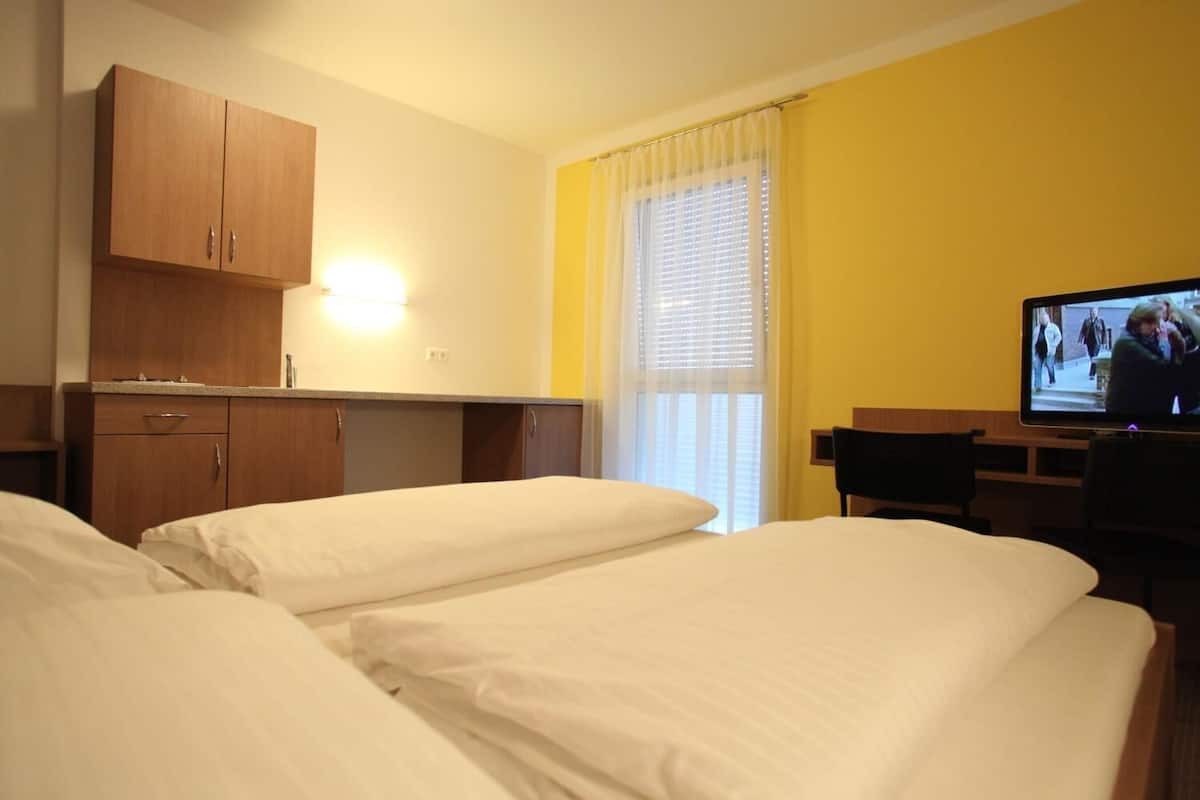 Ein Hotelzimmer mit zwei Betten, einem Fernseher, einem Schreibtisch und einem Fenster mit Jalousien.