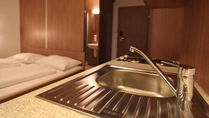 A compact hotel room with a single bed, a small sink, and a mirror.