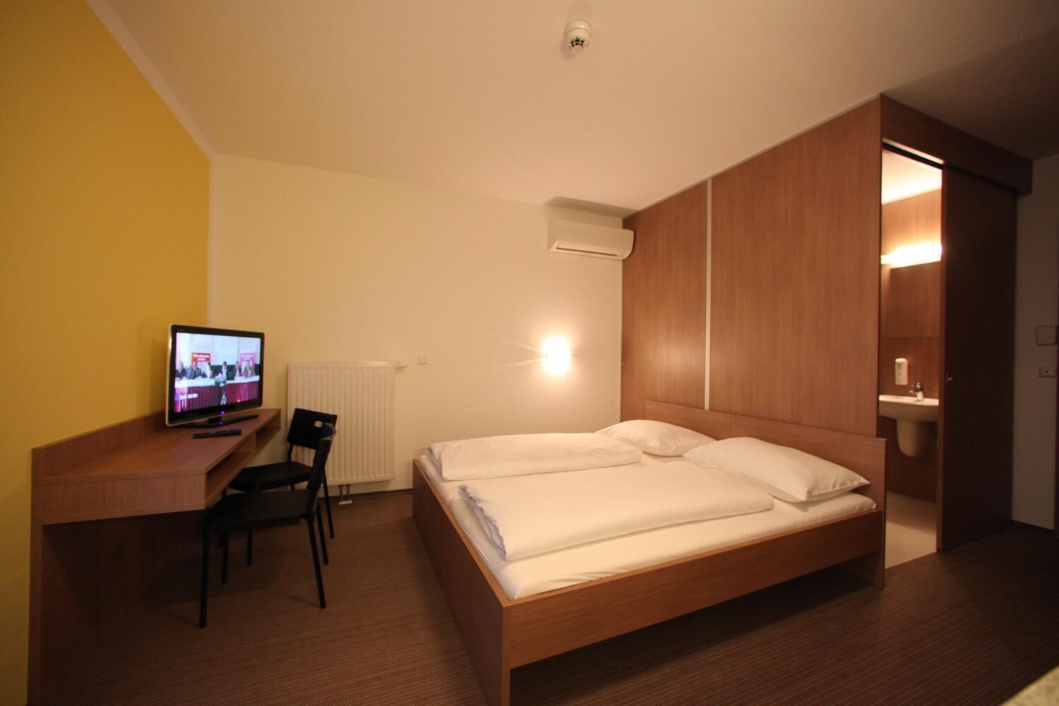 Una camera d'albergo con un letto, una scrivania con una sedia, una televisione e un bagno visibile attraverso una porta aperta.