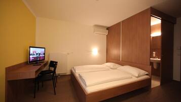 Una camera d'albergo con un letto, una scrivania con una sedia, una televisione e un bagno visibile attraverso una porta aperta.