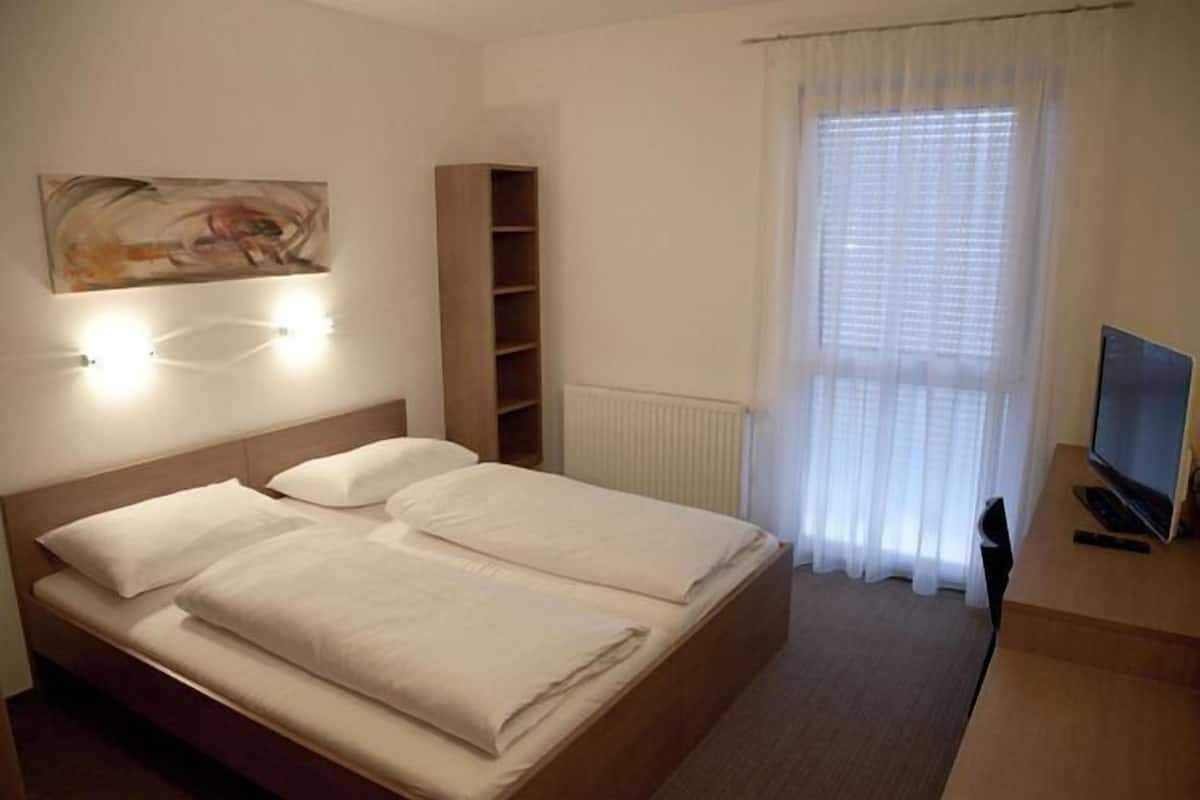 Ein Hotelzimmer mit einem Bett, einem Fernseher, einem Regal und einem Fenster mit Vorhängen.