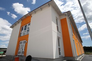 A two-story building with white and orange exterior walls, large windows, and a visible door. - Fair-Price-Hotel (Bad Waltersdorf)