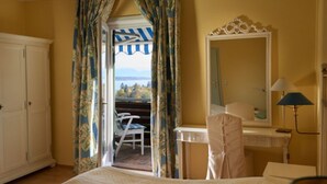 Habitación de hotel con cama, escritorio, silla, espejo y vistas al exterior.