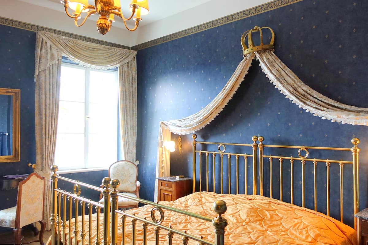A bedroom with a four-poster bed, ornate curtains, and a chandelier.