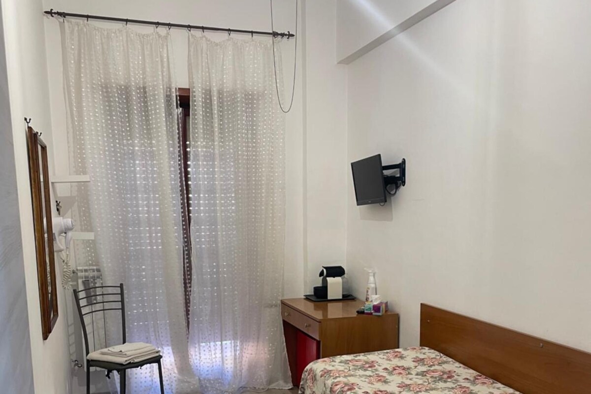 Un dormitorio con cama, escritorio, silla, televisor y ventana con cortinas.