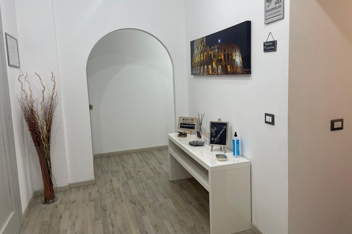 A hotel reception area with a white reception desk, a framed picture of a building, a signboard, and a decorative plant.