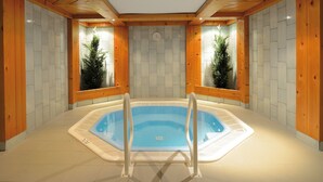 Un bain à remous dans un chalet en bois, avec des murs carrelés et des poutres apparentes.