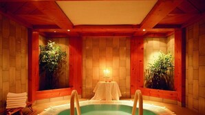 Un bain à remous avec une table et des chaises, situé dans une pièce en bois dont les murs sont recouverts de carreaux et où l’on trouve également des plantes.