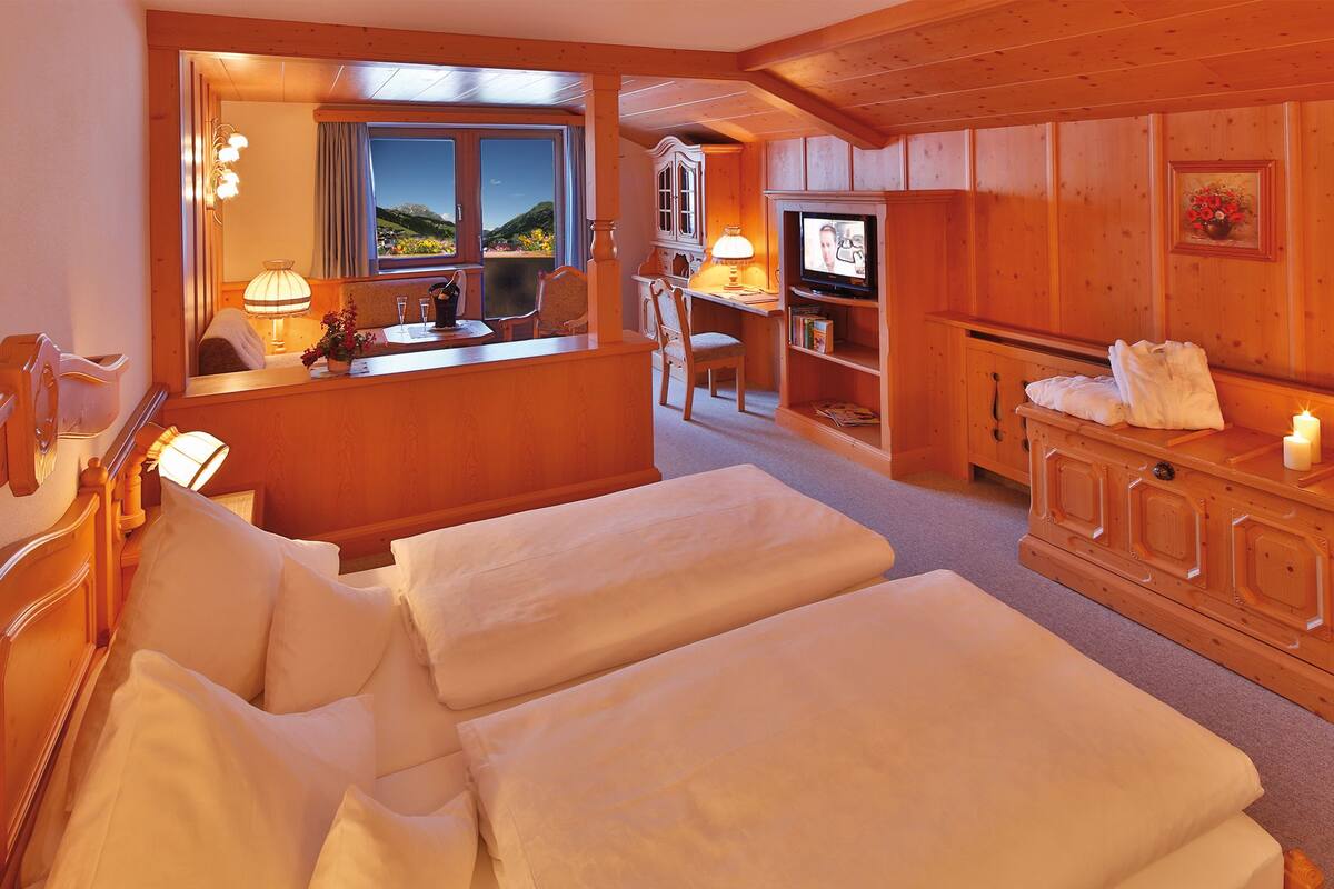 Habitación de hotel con dos camas, un escritorio con computadora, un televisor y ventana con vista a las montañas.
