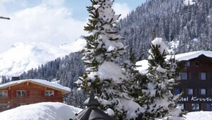 Un espace extérieur enneigé, avec un mur en pierre, un banc en bois et un arbre recouvert de neige.