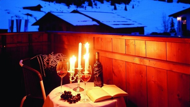 Une table dressée avec des verres à vin, une bougie et une bouteille, avec une vue sur les montagnes en arrière-plan.