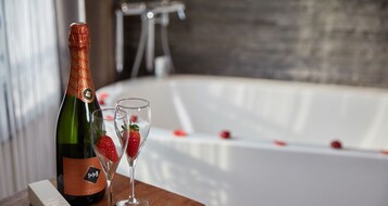 En champagneflaske og to glas med jordbær på et træbord, med et badekar i baggrunden.