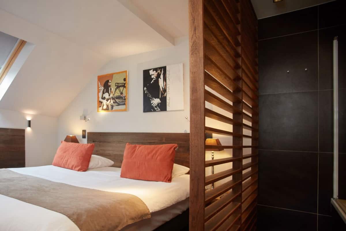 Une chambre à coucher comprenant un lit, deux oreillers, une tête de lit en bois, une table de chevet, deux lampes fixées au mur et deux affiches encadrées.
