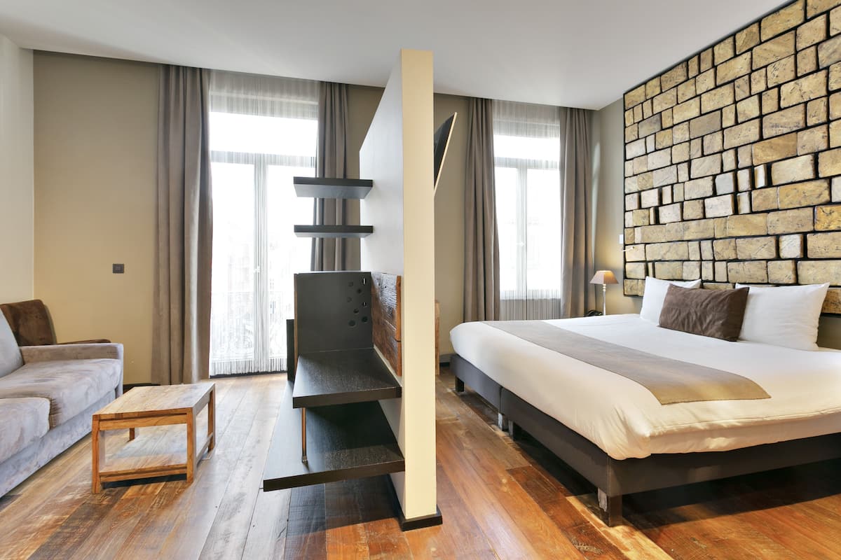 Une chambre d’hôtel moderne dotée d’un grand lit, d’une table basse en bois, d’une banquette intégrée et d’un mur décoratif au motif de briques.