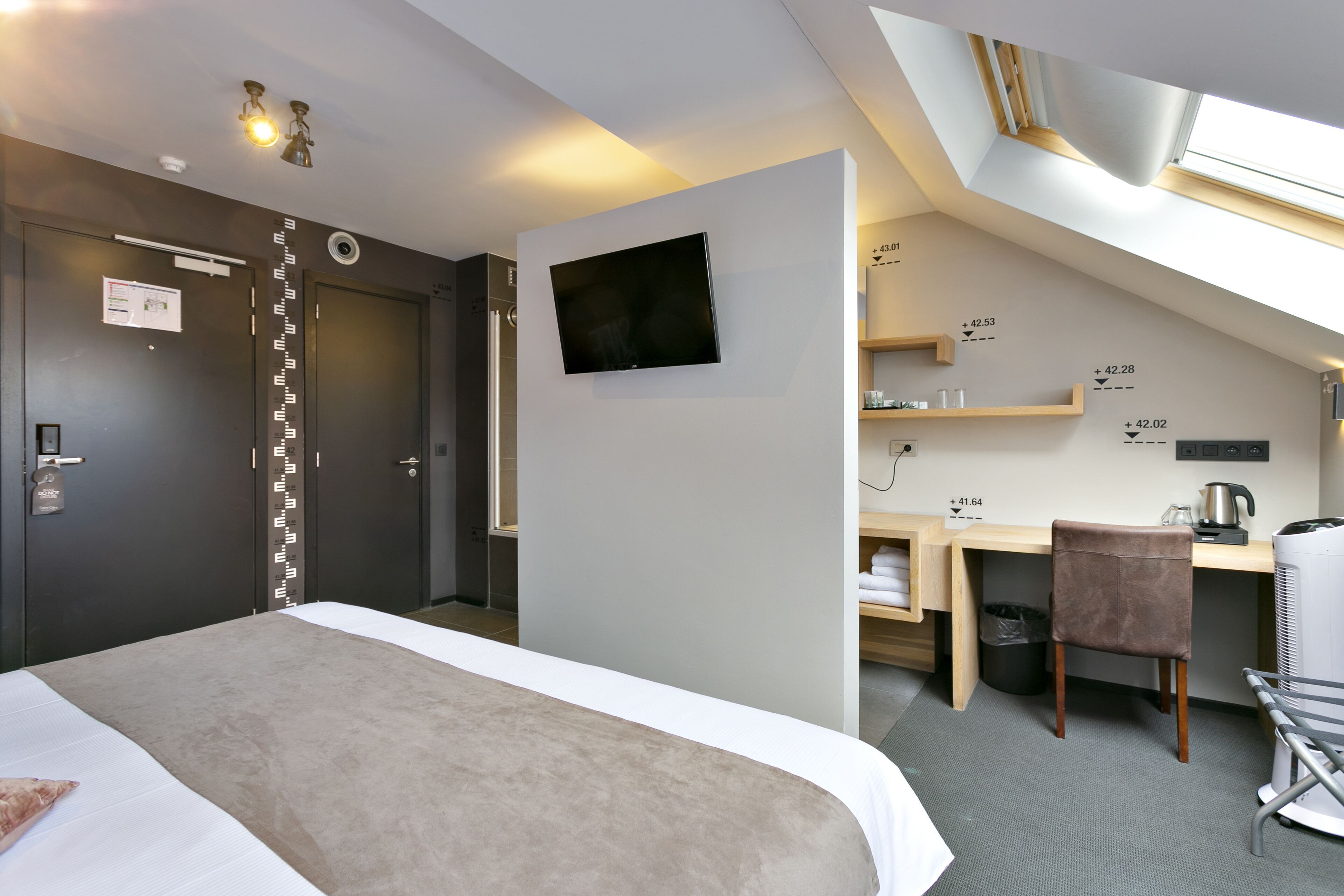 Una habitación de hotel moderna con cama, escritorio, silla, televisor y una pequeña kitchenette.