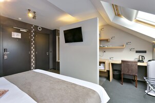 A modern hotel room with a bed, a desk, a chair, a TV, and a small kitchenette.