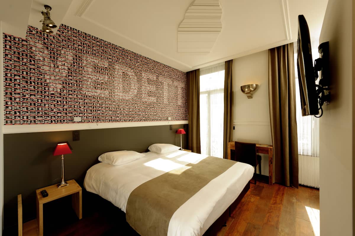 Une chambre d’hôtel avec un grand lit, un bureau, une télévision et un mur recouvert de photos.
