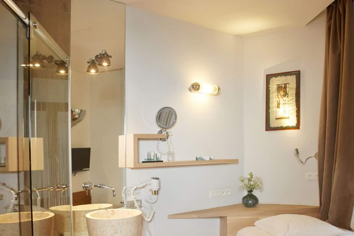 Une chambre d’hôtel comprenant un lit, une table de chevet, un miroir, un lavabo et un espace douche.