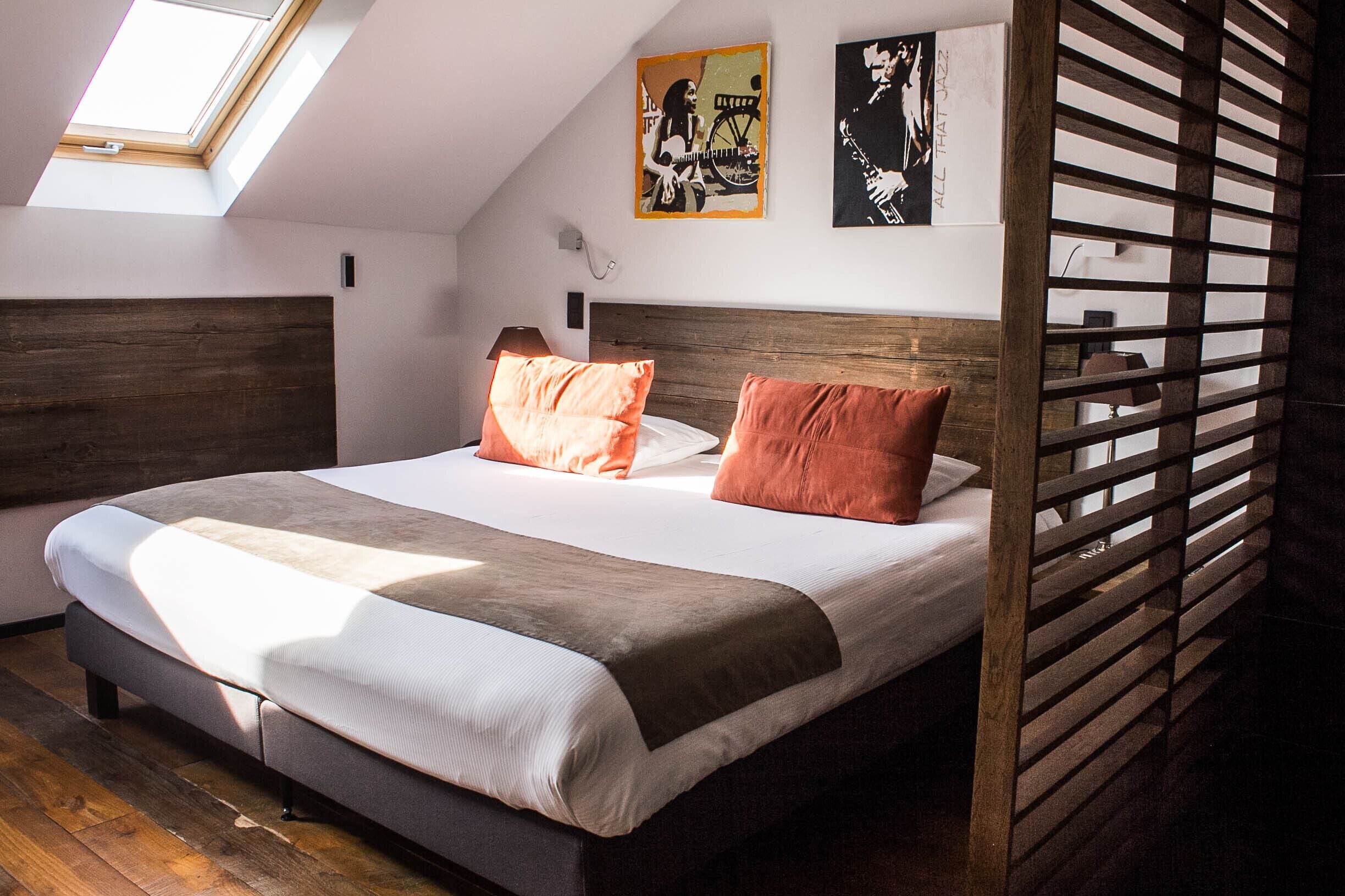 A bedroom with a sloped ceiling, a skylight, a bed with two pillows, and two wall-mounted artworks.